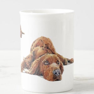 Peut inclure: Mug en céramique blanche avec une illustration à l'aquarelle d'un chien Setter irlandais brun couché. Le chien a des poils détaillés et des yeux expressifs. La tasse est de taille et de forme standard.