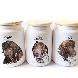 May include: Three white ceramic canisters with wooden lids. Each canister features a different dog breed with a watercolour illustration. The canisters are labelled "Sugar", "Coffee", and "Tea".
