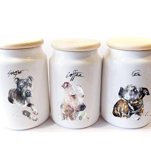 Peut inclure: Ensemble de trois bocaux en céramique blanche avec couvercles en bois. Chaque bocal est orné d'une peinture à l'aquarelle d'un chien et des mots "Sucre", "Café" et "Thé". Un ensemble de rangement de cuisine.