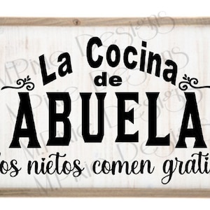 Peut inclure: Une pancarte en bois blanc avec du texte noir qui dit "La Cocina de ABUELA los nietos comen gratis". La pancarte a deux petits cœurs noirs de chaque côté du texte.