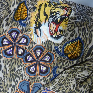 May include: A brown and beige leopard print fabric with colourful embroidered patches. The patches include a tiger face, a leaf, and several flower shapes.
