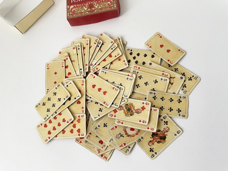 May include: A pile of playing cards with various suits and numbers, including hearts, clubs, diamonds, and spades. The cards are arranged in a random order, with some cards overlapping others. The cards are all in a cream color with red and black markings.