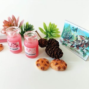 Op de afbeelding: Miniatuursc&egrave;ne met twee kleine glazen flesjes gevuld met roze vloeistof, met de labels "Pink Peony" en "Hearts & Kisses". De sc&egrave;ne bevat miniatuurkoekjes, dennenappels, een wenskaart met een winters tafereel en kunstmatige vetplanten. Het thema is een miniatuur cadeaupakket.