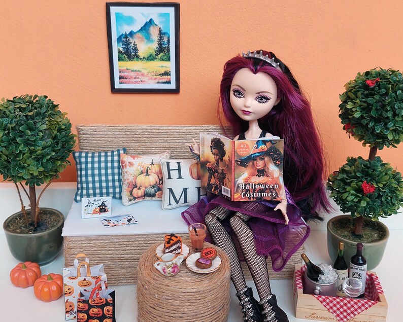 May include: A doll with purple hair and a purple dress reads a book titled "Halloween Costumes." The doll sits on a miniature couch with cushions. A small table holds treats and drinks, with miniature pumpkins and shopping bags nearby.