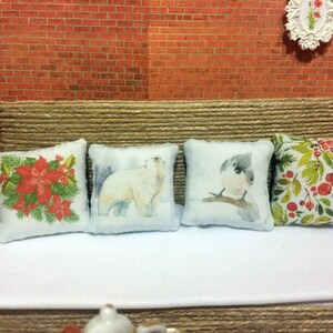 May include: Four decorative cushions with different designs. One cushion features red poinsettias and green leaves, another a polar bear in a snowy scene, a third a bird on a branch, and the last with red berries and green leaves.