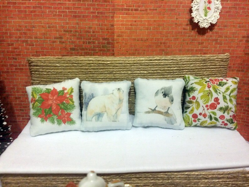 May include: Four decorative cushions with different designs. One cushion features red poinsettias and green leaves, another a polar bear in a snowy scene, a third a bird on a branch, and the last with red berries and green leaves.