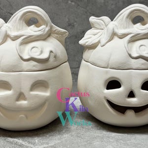 May include: Two white ceramic pumpkin candle holders with lids. The pumpkins have a carved jack-o'-lantern face and a stem with a leaf on top.