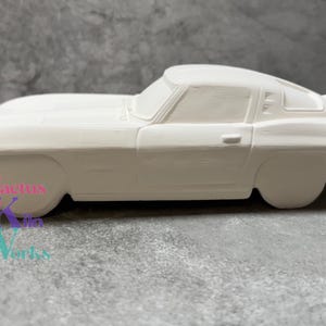 May include: White ceramic model of a classic car, a vintage Corvette, with a coupe body style. The car is unpainted and ready for customization.
