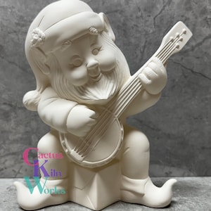 May include: A ceramic gnome figurine playing a banjo. The gnome is wearing a hat and boots. The figurine is unpainted and ready for customization. The text "Cactus Kiln Works" is visible on the base.