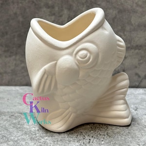 May include: A ceramic fish-shaped container in an off-white color. The container has a wide opening at the top and detailed fins and scales. The container is likely for holding small items or as a decorative piece.