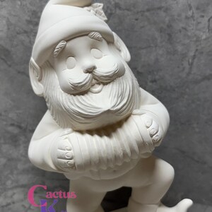 May include: A ceramic garden gnome figurine, unpainted and ready for customization. The gnome wears a tall hat and has a long beard, holding an accordion. The base of the figurine has the text "Cactus Kiln Works".