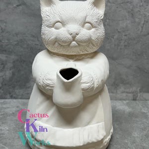 May include: White ceramic cat figurine holding a pitcher. The cat is wearing a dress and has a sweet expression on its face.