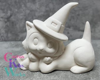 May include: White ceramic figurine of a cat wearing a witch hat. The cat is lying down with its paws tucked under its chin. The figurine is unpainted and ready to be decorated.