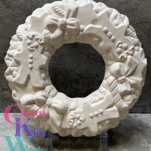 May include: A white ceramic Christmas wreath with embossed gingerbread men, bows, and candy canes. The wreath is displayed on a clear stand against a gray background. The wreath is unpainted and ready for customization.