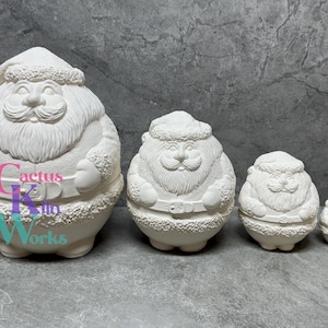 May include: Set of four white ceramic Santa Claus figurines of varying sizes. The largest Santa is holding a sack and has a beard and a hat. The figurines are unpainted and ready to be decorated.