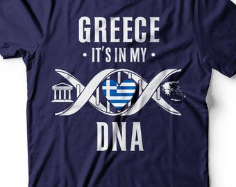 May include: Navy blue t-shirt with a white graphic design. The graphic features a DNA strand with a heart containing the Greek flag. The text "Greece, It's in my DNA" is printed on the shirt.
