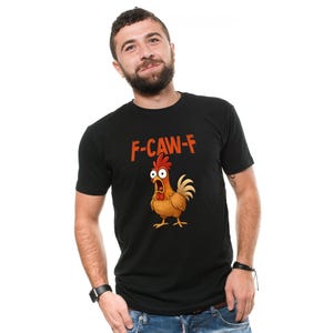 May include: Black t-shirt with the text "F-CAW-F" in orange letters above a cartoon chicken with a surprised expression. The chicken is brown, yellow, and red. The t-shirt is short-sleeved.