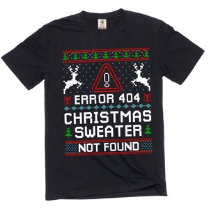 May include: Black t-shirt featuring a festive pixelated design. The text reads "ERROR 404 CHRISTMAS SWEATER NOT FOUND" with reindeer, Christmas trees, and a red warning sign. The shirt has a crew neck and short sleeves.