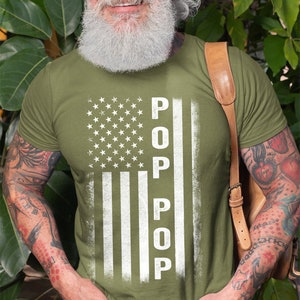 May include: A green t-shirt with a white distressed American flag design. The flag has the word "POP" written vertically down the middle.