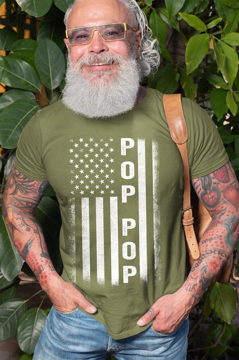 May include: A green t-shirt with a white distressed American flag design. The flag has the word "POP" written vertically down the middle.