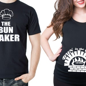 May include: Two black t-shirts with white text. The first shirt says "The Bun Baker" with a chef's hat graphic. The second shirt says "Bun in the Oven" with a graphic of a brick oven and a loaf of bread.