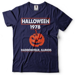 K&ouml;nnte beinhalten: Ein marineblaues T-Shirt mit einem wei&szlig;en Grafikdruck, auf dem "HALLOWEEN 1978 HADDONFIELD, ILLINOIS" steht, mit einem verwitterten orangefarbenen K&uuml;rbis in der Mitte.