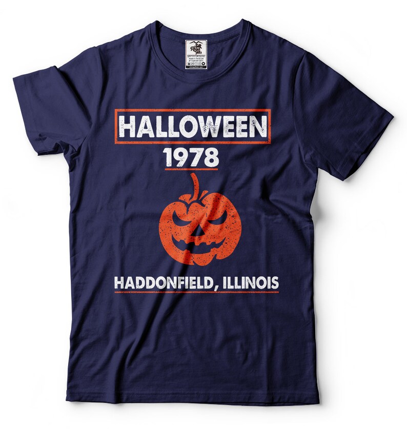 K&ouml;nnte beinhalten: Ein marineblaues T-Shirt mit einem wei&szlig;en Grafikdruck, auf dem "HALLOWEEN 1978 HADDONFIELD, ILLINOIS" steht, mit einem verwitterten orangefarbenen K&uuml;rbis in der Mitte.