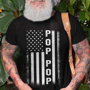May include: A black t-shirt with a white distressed American flag design. The word "POP" is written vertically down the flag.
