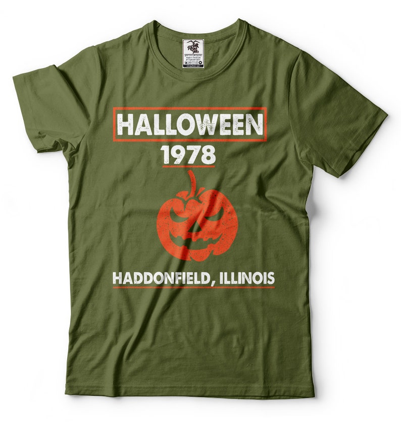 K&ouml;nnte beinhalten: Gr&uuml;nes T-Shirt mit einer wei&szlig;en Grafik, auf der "HALLOWEEN 1978 HADDONFIELD, ILLINOIS" steht, mit einem roten und orangefarbenen K&uuml;rbis in der Mitte.