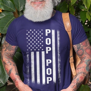 May include: A navy blue t-shirt with a white distressed American flag design and the word "POP" vertically down the right side of the flag.