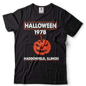 K&ouml;nnte beinhalten: Schwarzes T-Shirt mit einer wei&szlig;en Grafik, auf der "HALLOWEEN 1978" mit einem K&uuml;rbis in der Mitte und "HADDONFIELD, ILLINOIS" unter dem K&uuml;rbis steht.