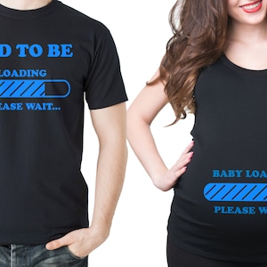 May include: Two black t-shirts with blue text and graphics. The first shirt says "Dad to be" with a blue progress bar that says "Loading... Please wait..." The second shirt says "Baby Loading... Please wait..." with a blue progress bar and two blue footprints.