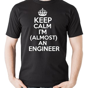 Pode incluir: Camiseta preta com texto branco que diz "Keep Calm I'm (Almost) An Engineer" com uma coroa acima do texto.