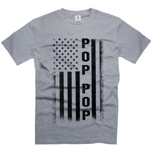 May include: A grey t-shirt with a distressed American flag design and the word "POP" written vertically in black.