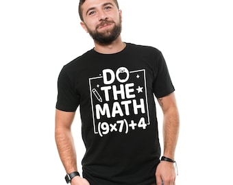 May include: Black t-shirt with the text "DO THE MATH (9x7)+4" in a white rectangular box. The design includes an apple, a pencil, and a star. The person in the image is wearing blue jeans and a black watch.