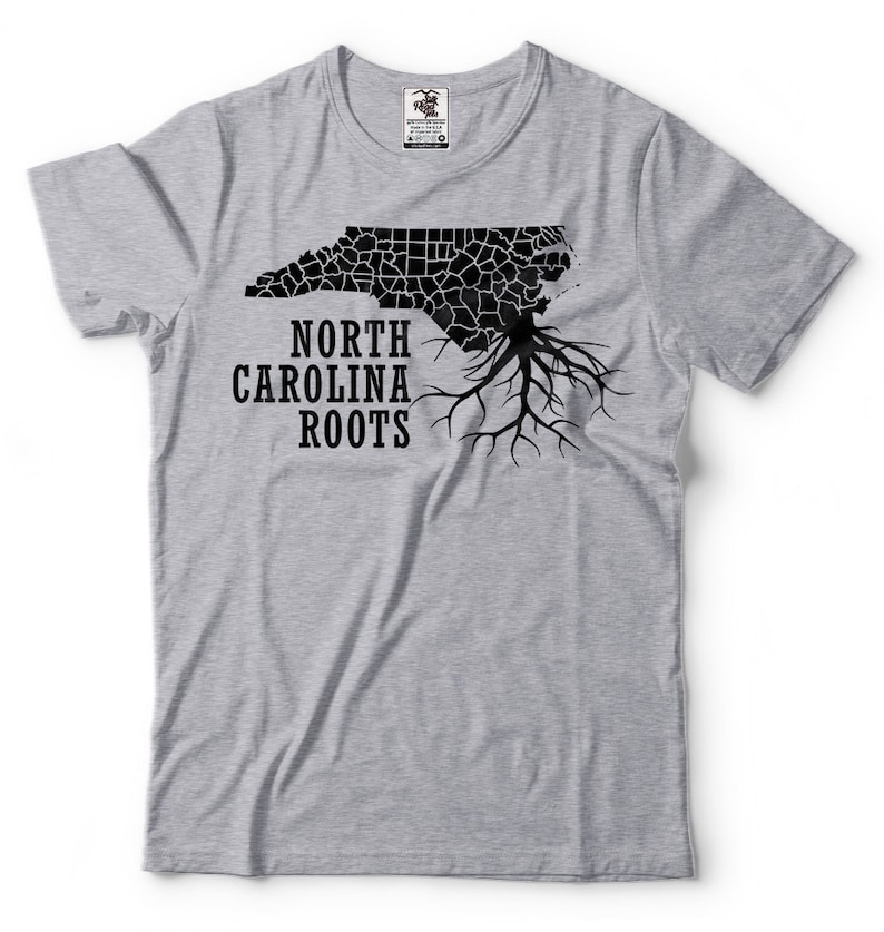 Puede incluir: Una camiseta gris con un contorno negro del estado de Carolina del Norte y las palabras "North Carolina Roots" impresas en ella.