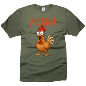 May include: Olive green t-shirt featuring a cartoon chicken with an open beak and the text "F-CAW-F" in red. The chicken has red comb and wattle, with a tan body and yellow feet.