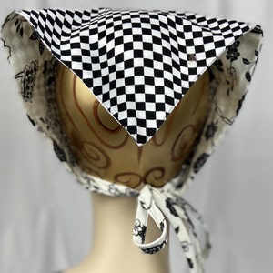 May include: A black and white checkered bonnet with a floral patterned lining. The bonnet is tied with matching fabric ties. A small metal emblem is visible on the front. The bonnet is displayed on a mannequin head.