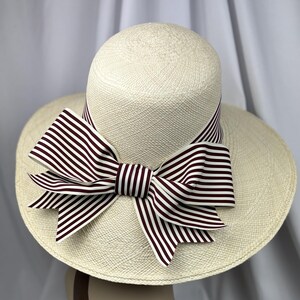 Pu&ograve; includere: Un cappello da sole color crema con tesa larga e corona arrotondata. Il cappello presenta un grande fiocco realizzato in tessuto a righe bianche e bordeaux. Il fiocco &egrave; centrato sul cappello e aggiunge un elemento decorativo al design.