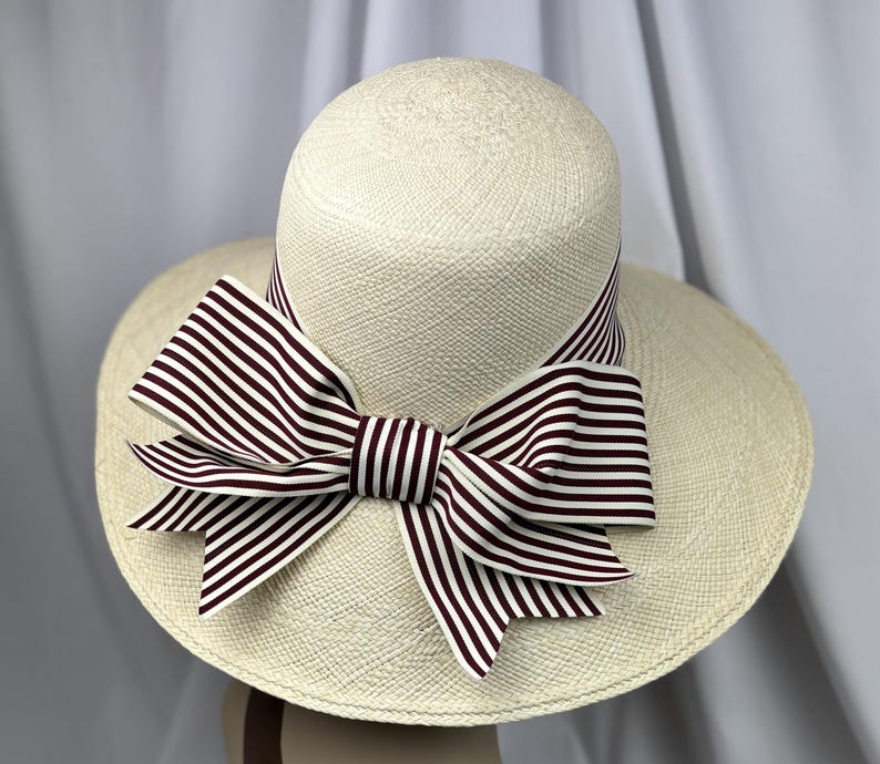 Pu&ograve; includere: Un cappello da sole color crema con tesa larga e corona arrotondata. Il cappello presenta un grande fiocco realizzato in tessuto a righe bianche e bordeaux. Il fiocco &egrave; centrato sul cappello e aggiunge un elemento decorativo al design.