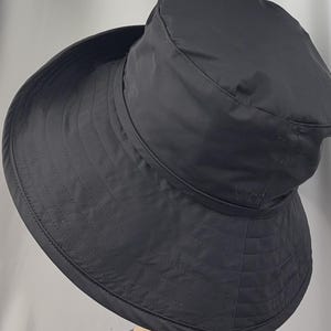 Pu&ograve; includere: Un cappello nero a tesa larga con un motivo trapuntato. Il cappello presenta una corona arrotondata e un'ampia tesa rivolta verso il basso. Il cappello &egrave; realizzato in un materiale liscio, possibilmente resistente all'acqua, ed &egrave; progettato per la protezione solare.