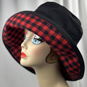 Pu&ograve; includere: Cappello da pescatore nero con fodera a quadri rossi e neri. Il cappello ha un'ampia tesa ed &egrave; esposto su una testa di manichino. &Egrave; un accessorio elegante.