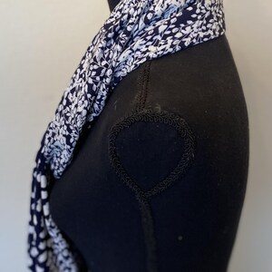 May include: A white and navy blue scarf with a floral pattern. The scarf is folded and draped around a black mannequin.