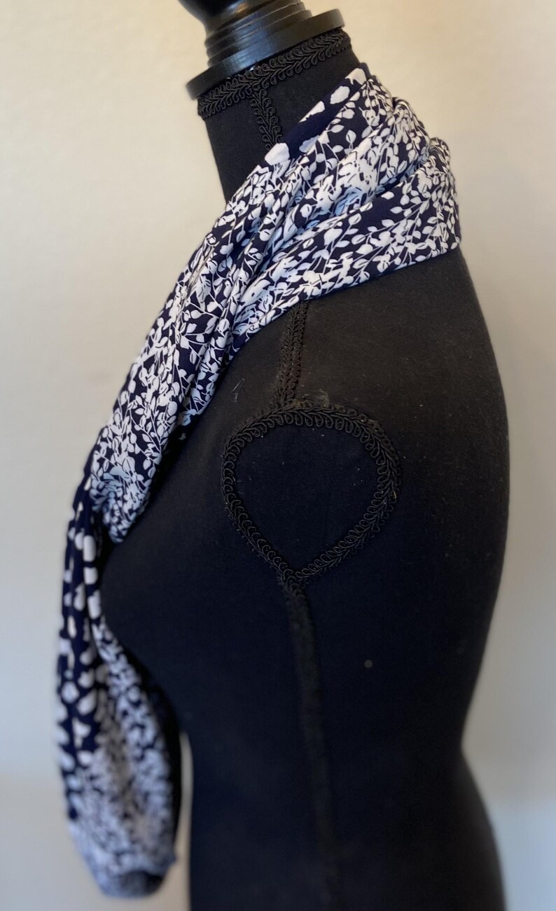 May include: A white and navy blue scarf with a floral pattern. The scarf is folded and draped around a black mannequin.