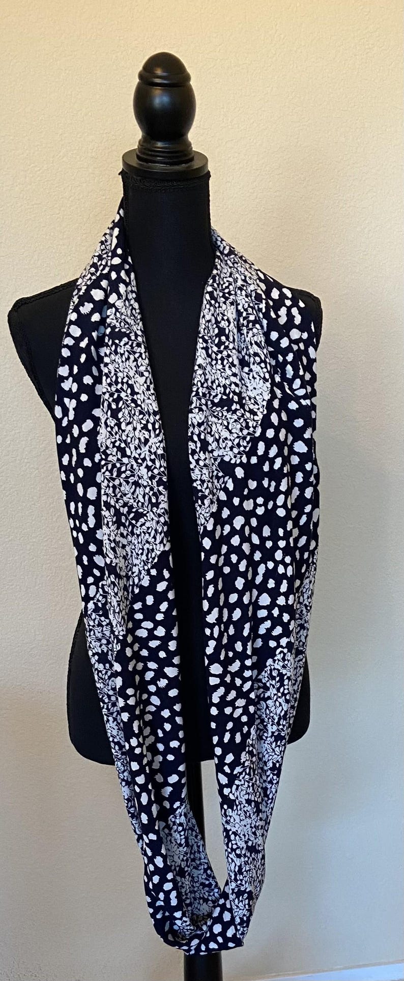 May include: A black and white infinity scarf with a floral and polka dot pattern.