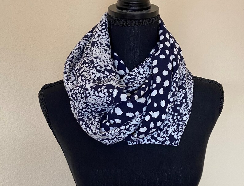 May include: A navy blue and white patterned infinity scarf. The scarf has a floral design on one side and a polka dot design on the other side.