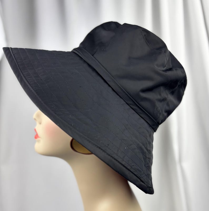 Pu&ograve; includere: Cappello da sole nero con tesa larga e fascia intorno alla corona. Il cappello &egrave; realizzato in un materiale liscio. La tesa ha un design cucito. Un accessorio elegante per la protezione solare.