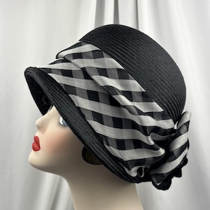 May include: A black cloche hat with a wide brim and a decorative band. The band features a black and white checked pattern, offering a vintage aesthetic. This hat is a fashionable accessory.
