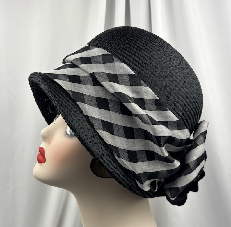 May include: A black cloche hat with a wide brim and a decorative band. The band features a black and white checked pattern, offering a vintage aesthetic. This hat is a fashionable accessory.