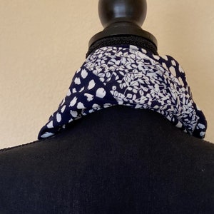 May include: A black and white patterned scarf with a floral design. The scarf is tied around a black mannequin's neck.